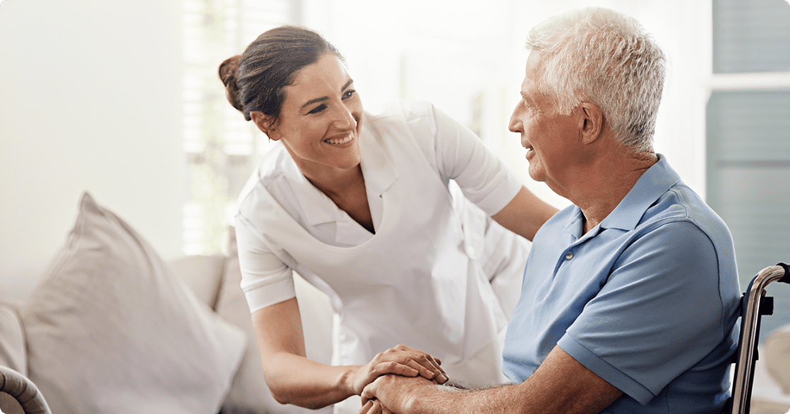 Nurse smiling at elderly man in wheelchair.