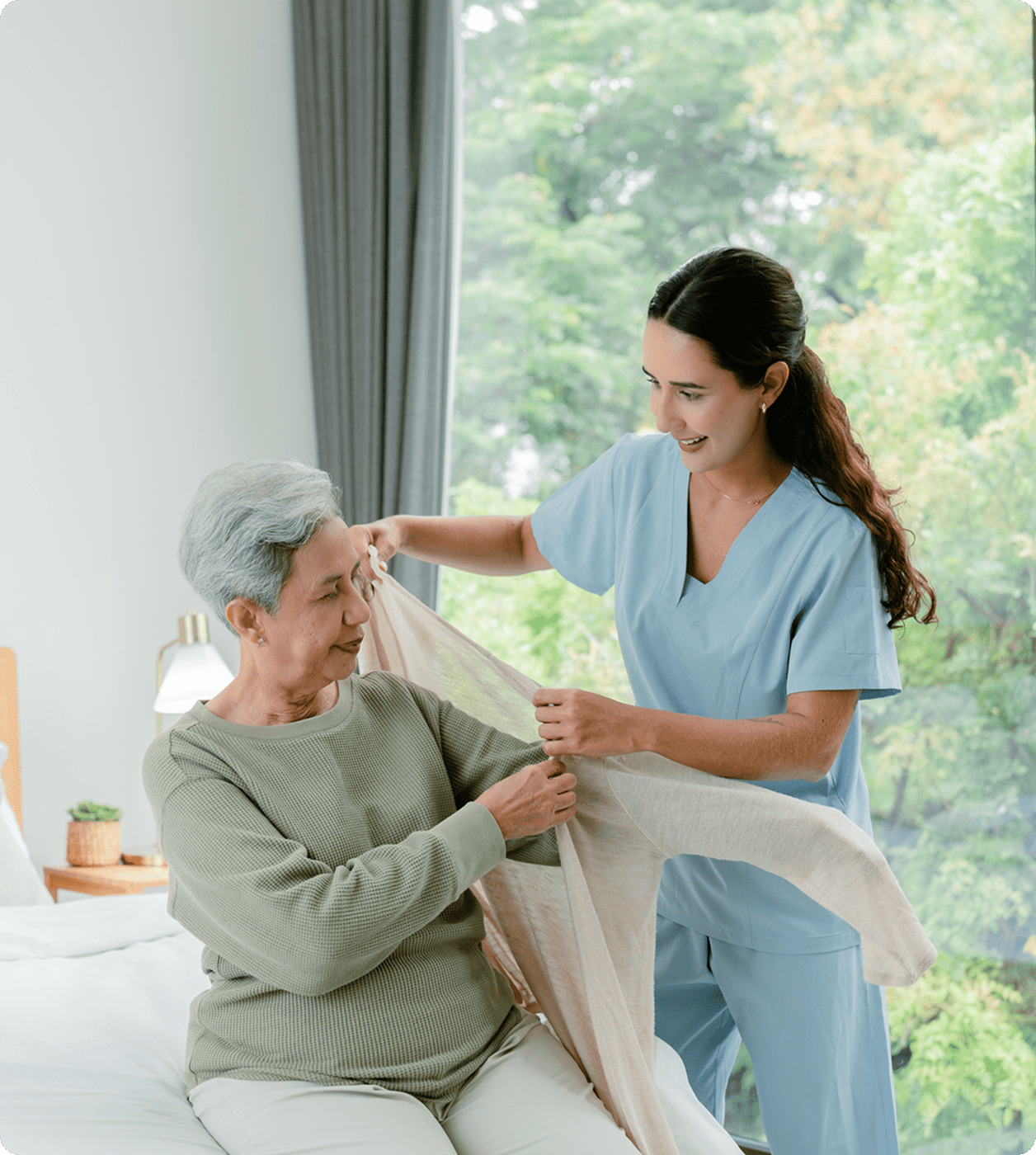 Caregiver assisting elderly woman with clothing.